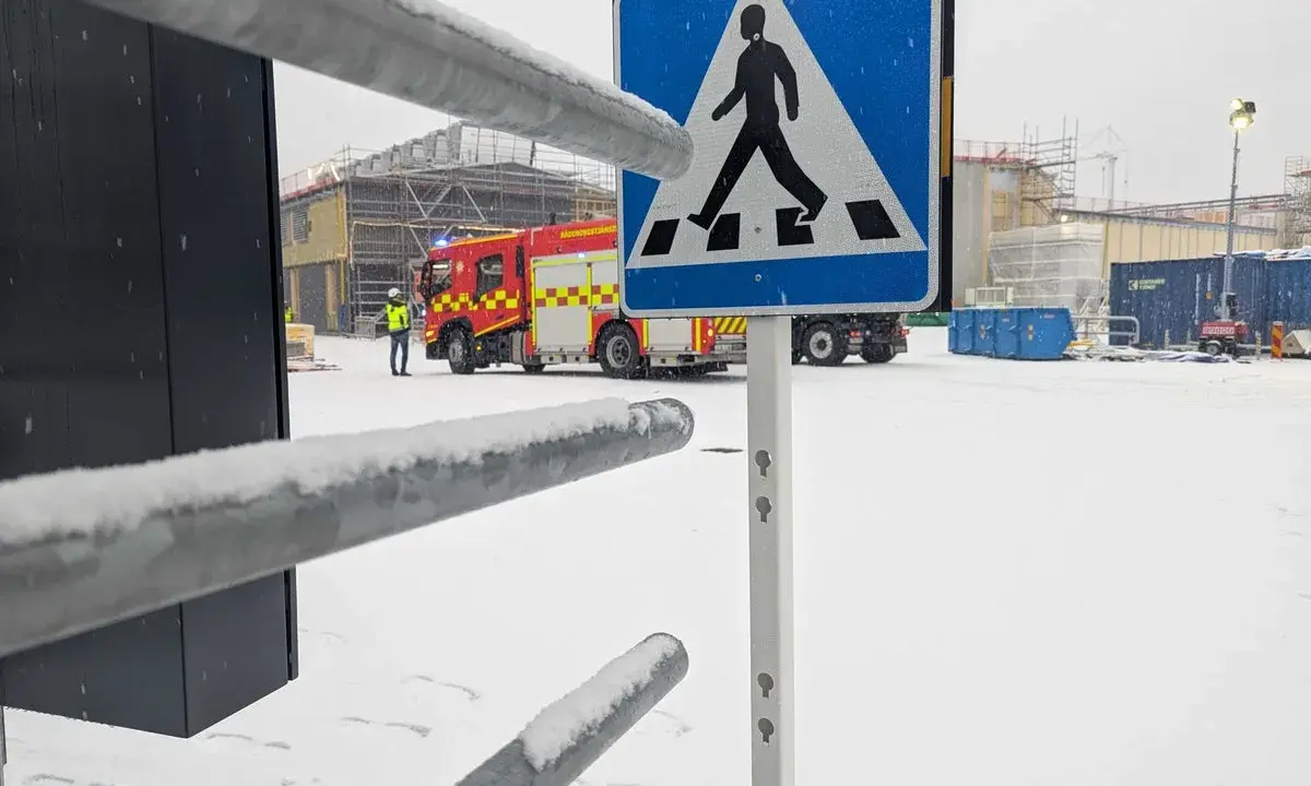 Snöig arbetsplats med brandbil och en person i varselväst. En övergångsställe-skylt står framför. Kanske en leveransbesiktning brandlarm pågår.