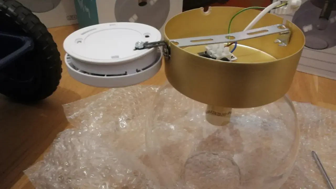 SBF 110:8 lampdelar, inklusive en guldfärgad takkopp och en vit bas, ligger på bubbelplast.