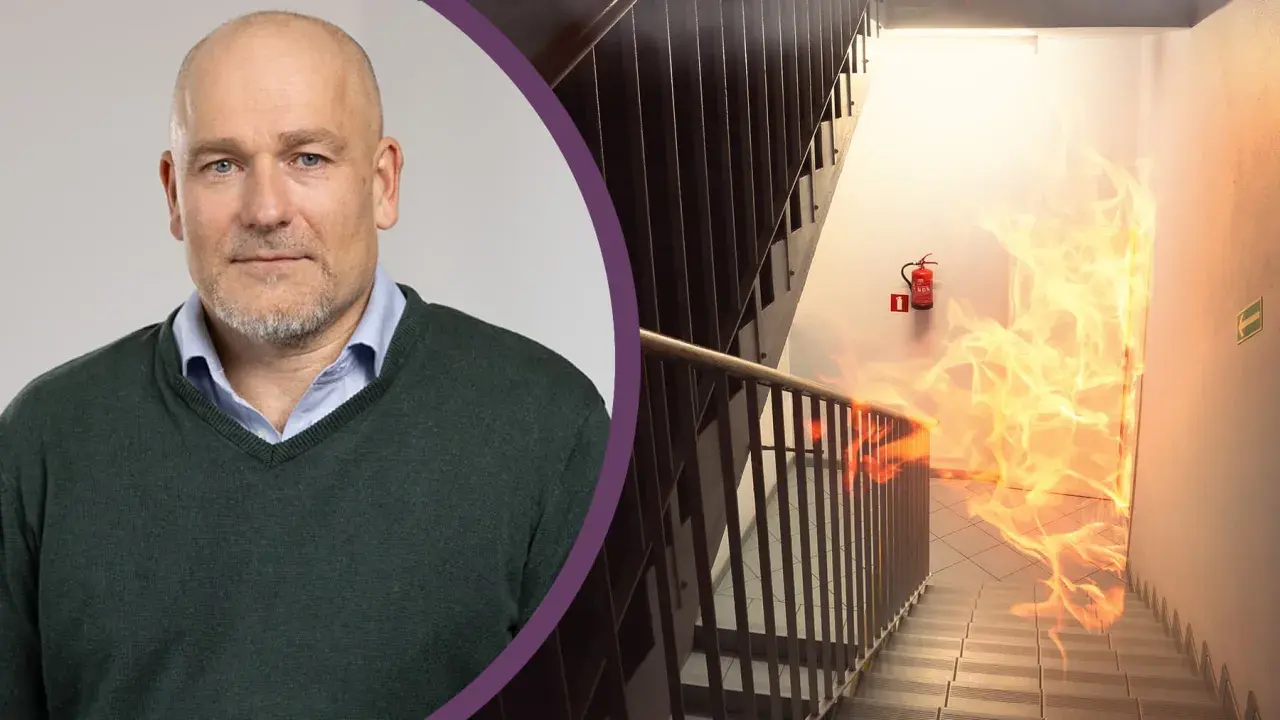 Man med skägg och en brandhärjad trappa med brandsläckare. Viktigt med revisionsbesiktning brandlarm för säkerheten.