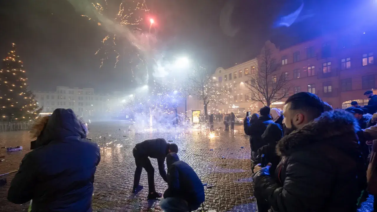 Folk ser på fyrverkerier olagligt på en stadsgata med julgran och byggnader.
