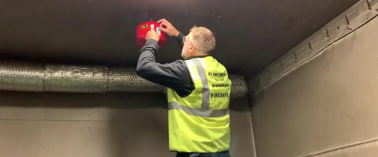 Man i varselväst installerar en brandsläckare i ett utomhus soprum.