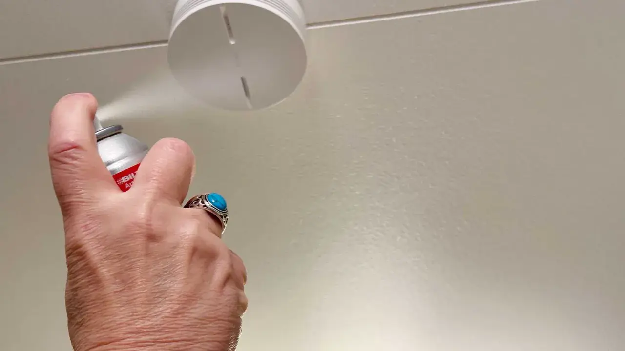 En hand sprayar en uppkopplad brandvarnare i taket.
