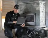 Sotare med laptop vid eldstad. Regelbunden brandskyddskontroll hur ofta är viktig för säkerheten.