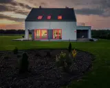 Modern villa brand med lysande röda fönsterramar mot en dramatisk solnedgång.