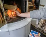 En hand tänder eld i en kakelugn med vedträn som väntar på att värmas.