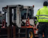 Arbetare i varseljacka inspekterar en truckladdning med flera gaffeltruckar i bakgrunden.