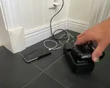 En hand placerar ett litiumbatteri på en laddare. En mobiltelefon laddas bredvid.