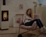 En kvinna stickar i en mysig fåtölj bredvid en sprakande kamin. Frågan är hur varmt blir det i en kamin?