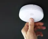 En hand trycker på en brandvarnare som piper trots nytt batteri.