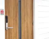 En modern ytterdörr med ett Yale Doorman Classic vs V2N lås. Dörren är i trä och husfasaden är vit.