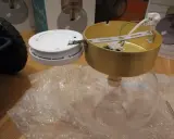 SBF 110:8 lampdelar, inklusive en guldfärgad takkopp och en vit bas, ligger på bubbelplast.