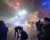 Folk ser på fyrverkerier olagligt på en stadsgata med julgran och byggnader.