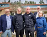 Fem personer står framför en byggnad. Två bär svarta träningsjackor med texten "GÖSAL". En man i blå kavaj och jeans, en kvinna i jeanskjol och en man i kostym. Kanske diskuterar de sotningskurs pris.
