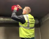 Man i varselväst installerar en brandsläckare i ett utomhus soprum.