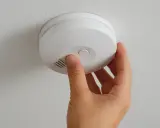 En hand trycker på testknappen för att byta batteri i brandvarnaren. Säkerhet först!