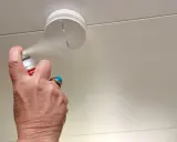 En hand sprayar en uppkopplad brandvarnare i taket.