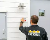 Man monterar en Verisure-larmdekal på husfasaden, en del av ett smart hem-system som kan integreras med Google Home.