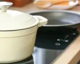 En person lagar mat på en induktionshäll med en kastrull och en stekpanna. En spisvakt kan förhindra olyckor genom att övervaka värmen.