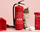 En katt spanar in en röd brandsläckare och en brandfilt. Ett litet rött hus står bredvid.