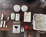 Säkerhetssystem från Sector Alarm, inklusive larmpanel, rörelsedetektorer, dörrsensorer och en tom larmcentral. Perfekt för en trygg home assistant.