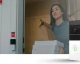 Säkerhetskameran vid dörren fångar en person med matleverans. En klisterlapp från Sector Alarm indikerar att hemmet är skyddat mot bedragare.