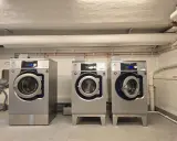Tre professionella torktumlare i metall. En varningssymbol för torktumlare brandrisk syns på en av maskinerna.