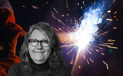 Kvinna med glasögon ler framför en bakgrund av gnistor från heta arbeten. En svetsare i skyddskläder syns till vänster.