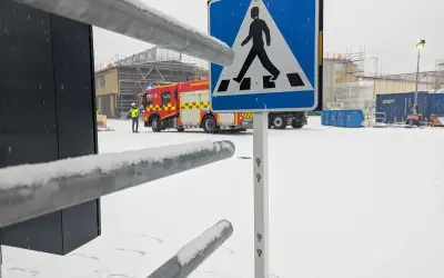 Snöig arbetsplats med brandbil och en person i varselväst. En övergångsställe-skylt står framför. Kanske en leveransbesiktning brandlarm pågår.