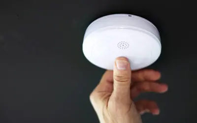 En hand trycker på en brandvarnare som piper trots nytt batteri.