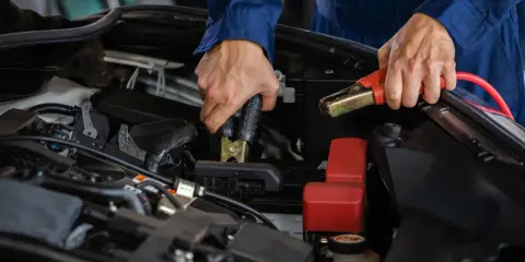 Person i blå overall kopplar startkablar för att ladda bilbatteri inomhus.