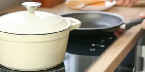 En person lagar mat på en induktionshäll med en kastrull och en stekpanna. En spisvakt kan förhindra olyckor genom att övervaka värmen.