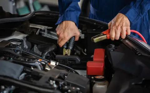 Person i blå overall kopplar startkablar för att ladda bilbatteri inomhus.