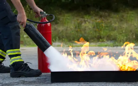 Person i skyddskläder släcker eld med brandsläckare. Praktisk brand utbildning för säkerhet.