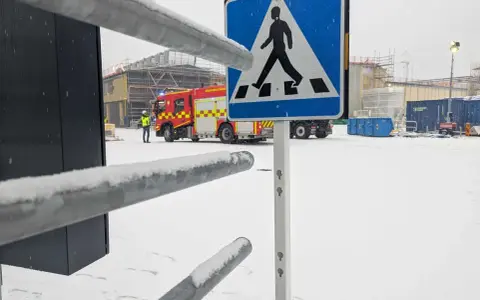Snöig arbetsplats med brandbil och en person i varselväst. En övergångsställe-skylt står framför. Kanske en leveransbesiktning brandlarm pågår.