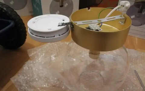 SBF 110:8 lampdelar, inklusive en guldfärgad takkopp och en vit bas, ligger på bubbelplast.