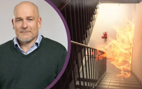 Man med skägg och en brandhärjad trappa med brandsläckare. Viktigt med revisionsbesiktning brandlarm för säkerheten.