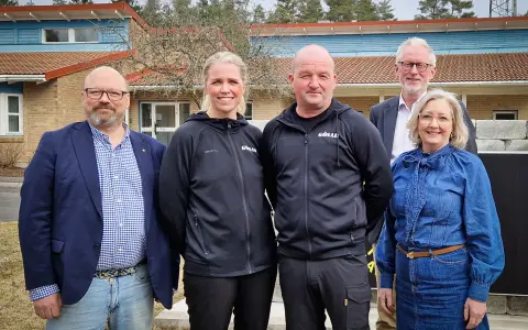 Fem personer står framför en byggnad. Två bär svarta träningsjackor med texten "GÖSAL". En man i blå kavaj och jeans, en kvinna i jeanskjol och en man i kostym. Kanske diskuterar de sotningskurs pris.