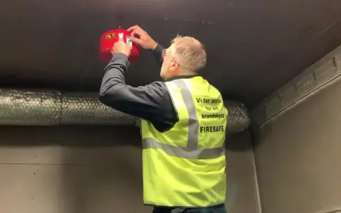 Man i varselväst installerar en brandsläckare i ett utomhus soprum.