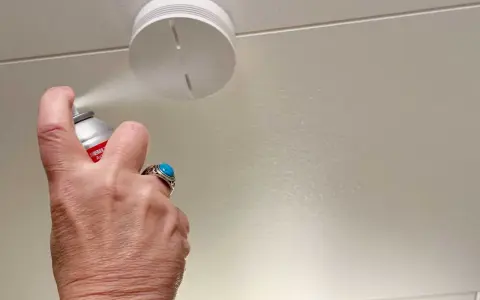 En hand sprayar en uppkopplad brandvarnare i taket.