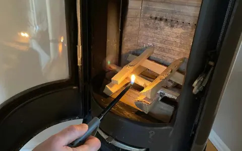 En hand tänder eld i kaminen med en lång tändare. Snart sprider sig värmen i rummet.