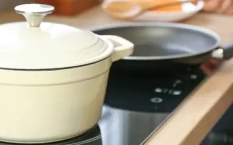 En person lagar mat på en induktionshäll med en kastrull och en stekpanna. En spisvakt kan förhindra olyckor genom att övervaka värmen.