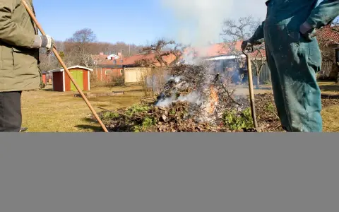 Två personer eldar trädgårdsavfall. Röken stiger mot en klarblå himmel.
