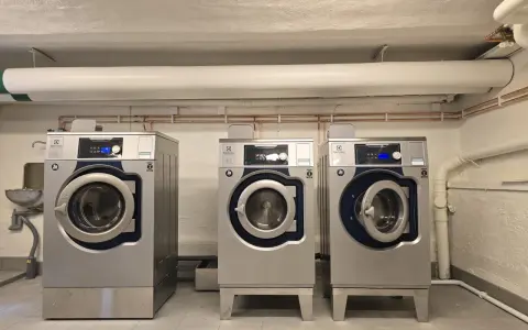 Tre professionella torktumlare i metall. En varningssymbol för torktumlare brandrisk syns på en av maskinerna.