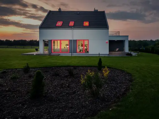 Modern villa brand med lysande röda fönsterramar mot en dramatisk solnedgång.