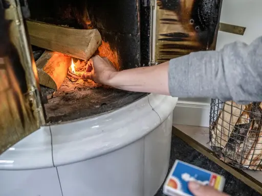 En hand tänder eld i en kakelugn med vedträn som väntar på att värmas.
