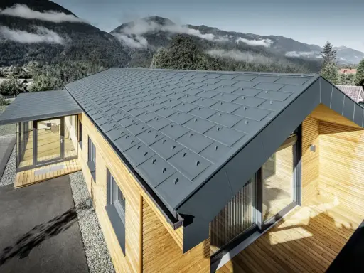 Modernt hus med grått plåttak, där åskledare diskret integrerats. Omgivet av berg och skog.