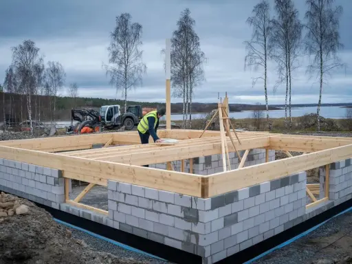 Byggnadsarbetare arbetar med grunden till ett hus, i enlighet med plan- och bygglagen. En maskin står i bakgrunden.