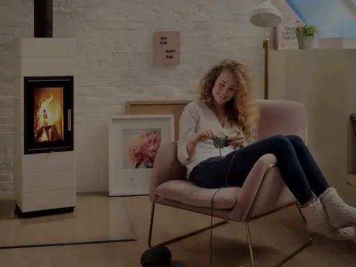 En kvinna stickar i en mysig fåtölj bredvid en sprakande kamin. Frågan är hur varmt blir det i en kamin?