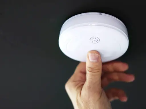 En hand trycker på en brandvarnare som piper trots nytt batteri.