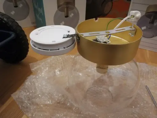 SBF 110:8 lampdelar, inklusive en guldfärgad takkopp och en vit bas, ligger på bubbelplast.